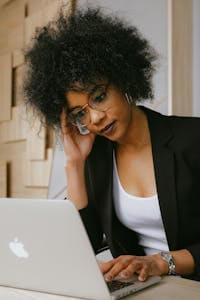 Businesswoman with afro hairstyle working on a laptop, looking focused and professional in an office setting.